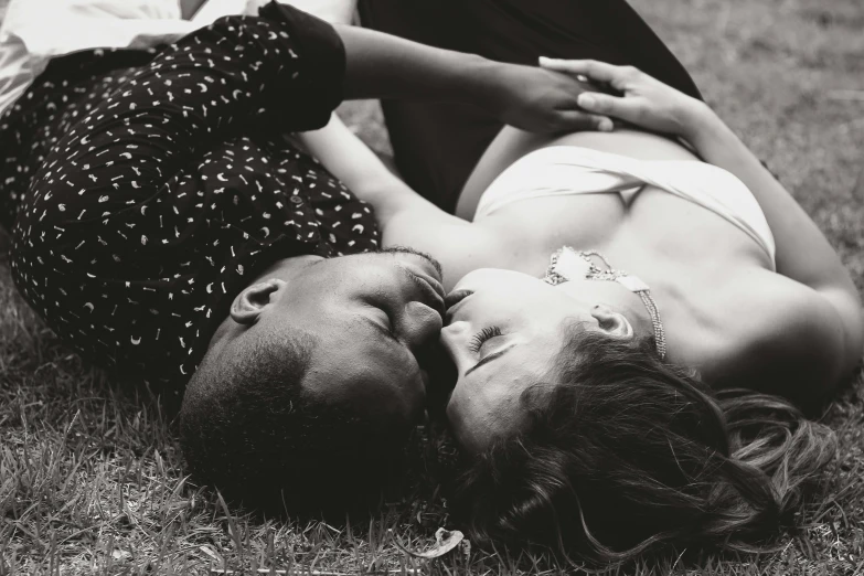 a woman in a white dress lays on the ground beside a man who is kissing her