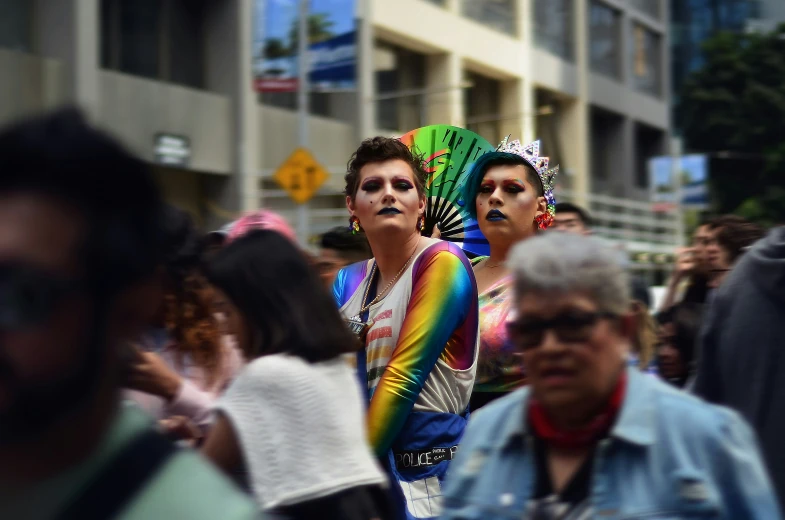 a man dressed in a gay pride outfit stands surrounded by people on the street