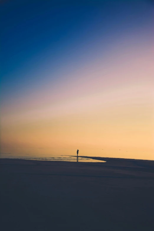 a person standing on a sandy beach watching the sun set