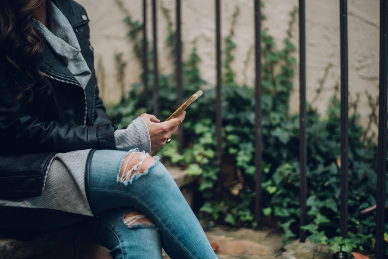 a person sits on a bench texting on her phone