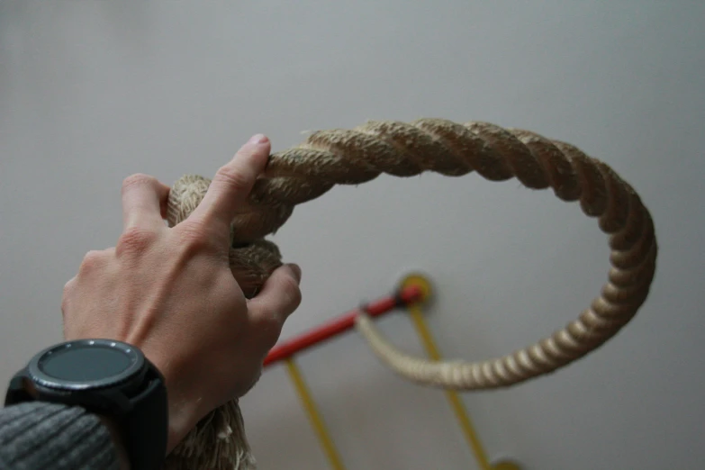 a hand reaching out towards a large rope with a watch on it