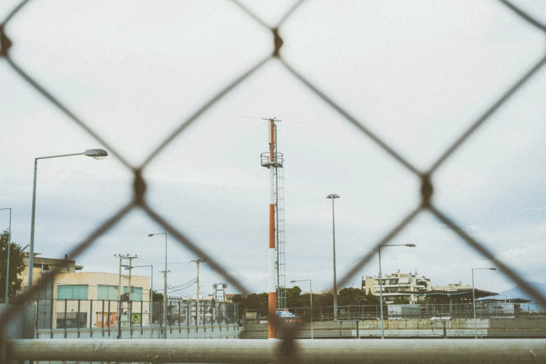 a very tall tv tower through a metal fence