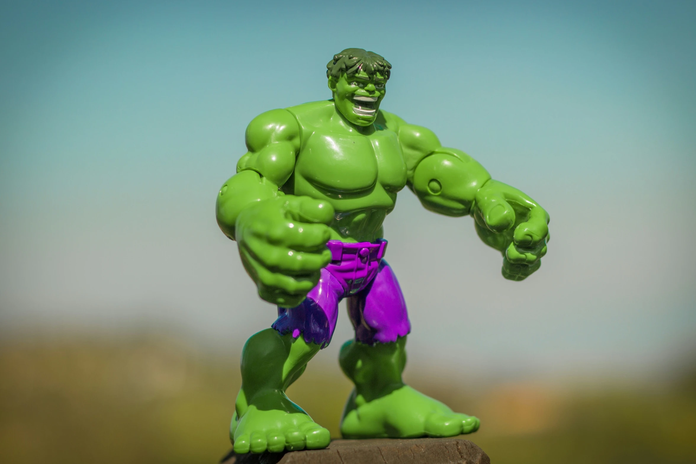 a toy hulk with a purple glove is in a grassy area