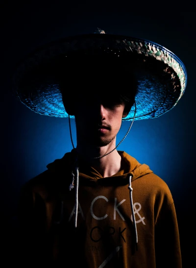 the man wearing a large sombrero stands in the shadows