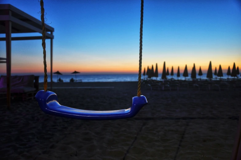 a blue and yellow swings at sunset with umbrellas in the background