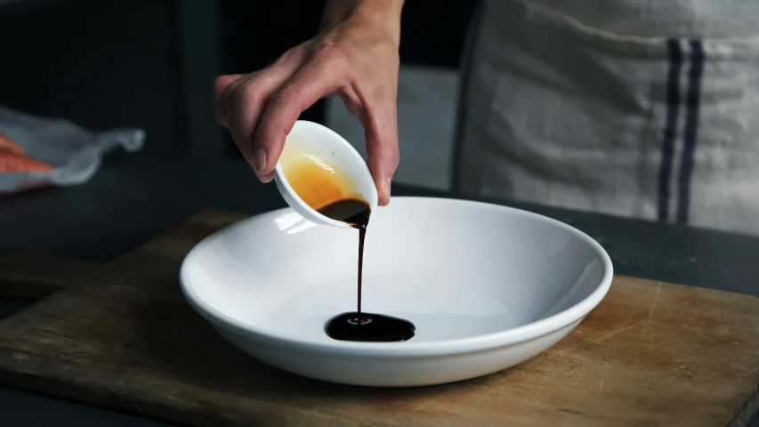 someone pours a sauce into a bowl on a wooden  board