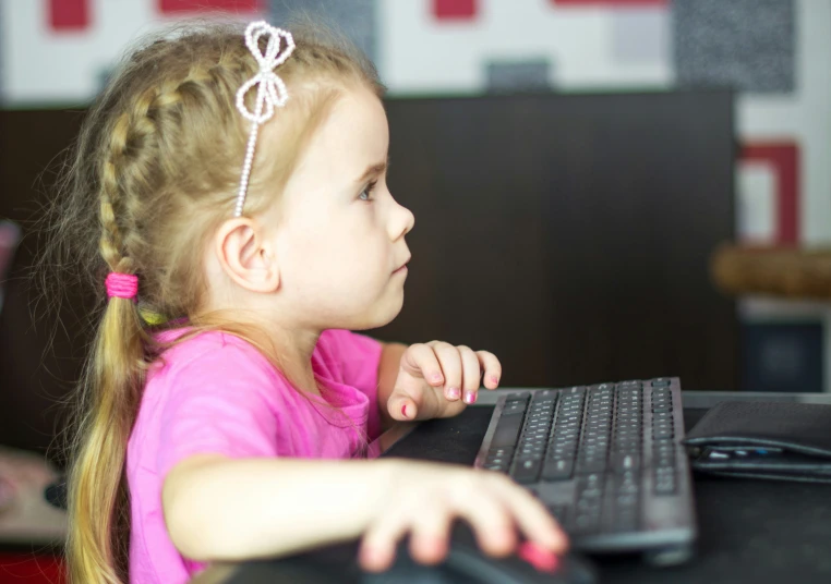 a little girl sitting at a computer with a keyboard