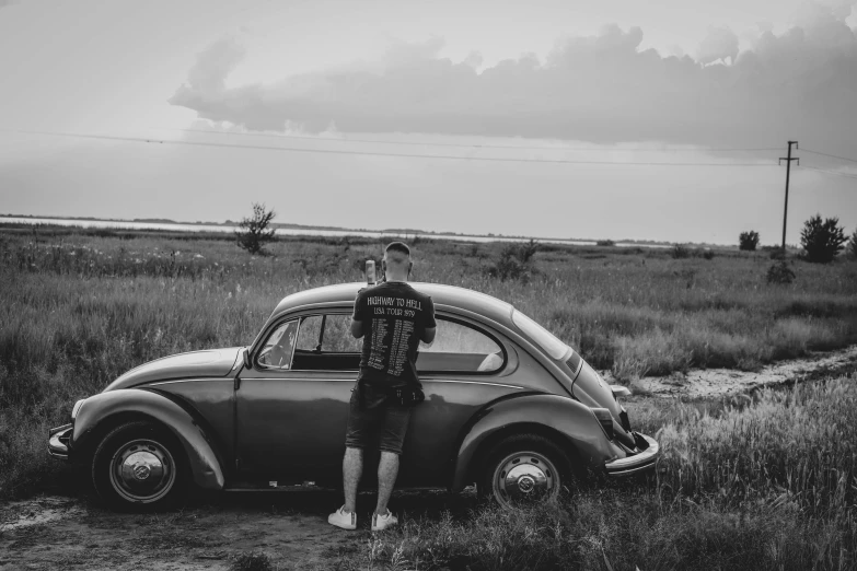 a man stands beside an old vw bug on a country road