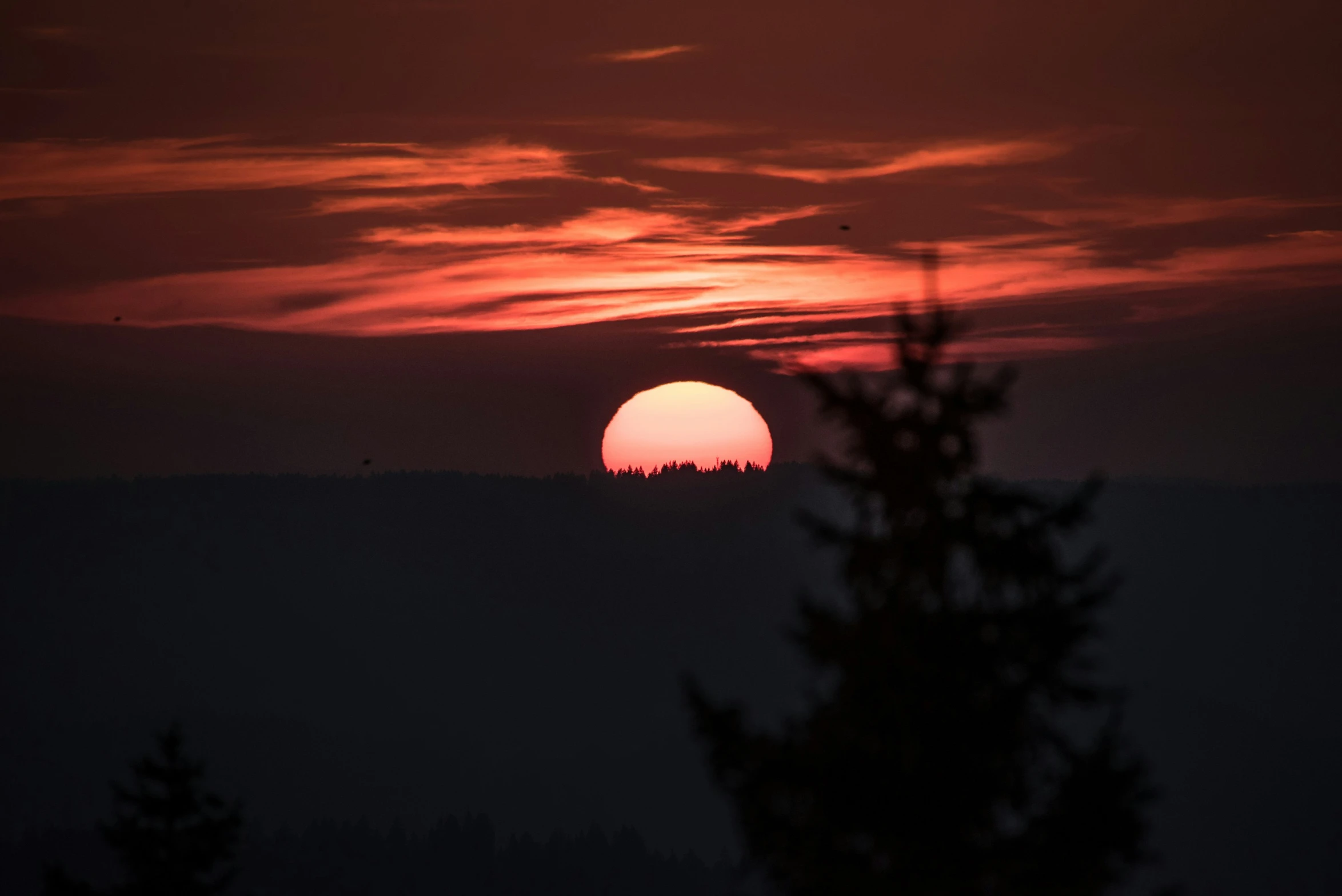 an orange ball of sun is setting over the hills