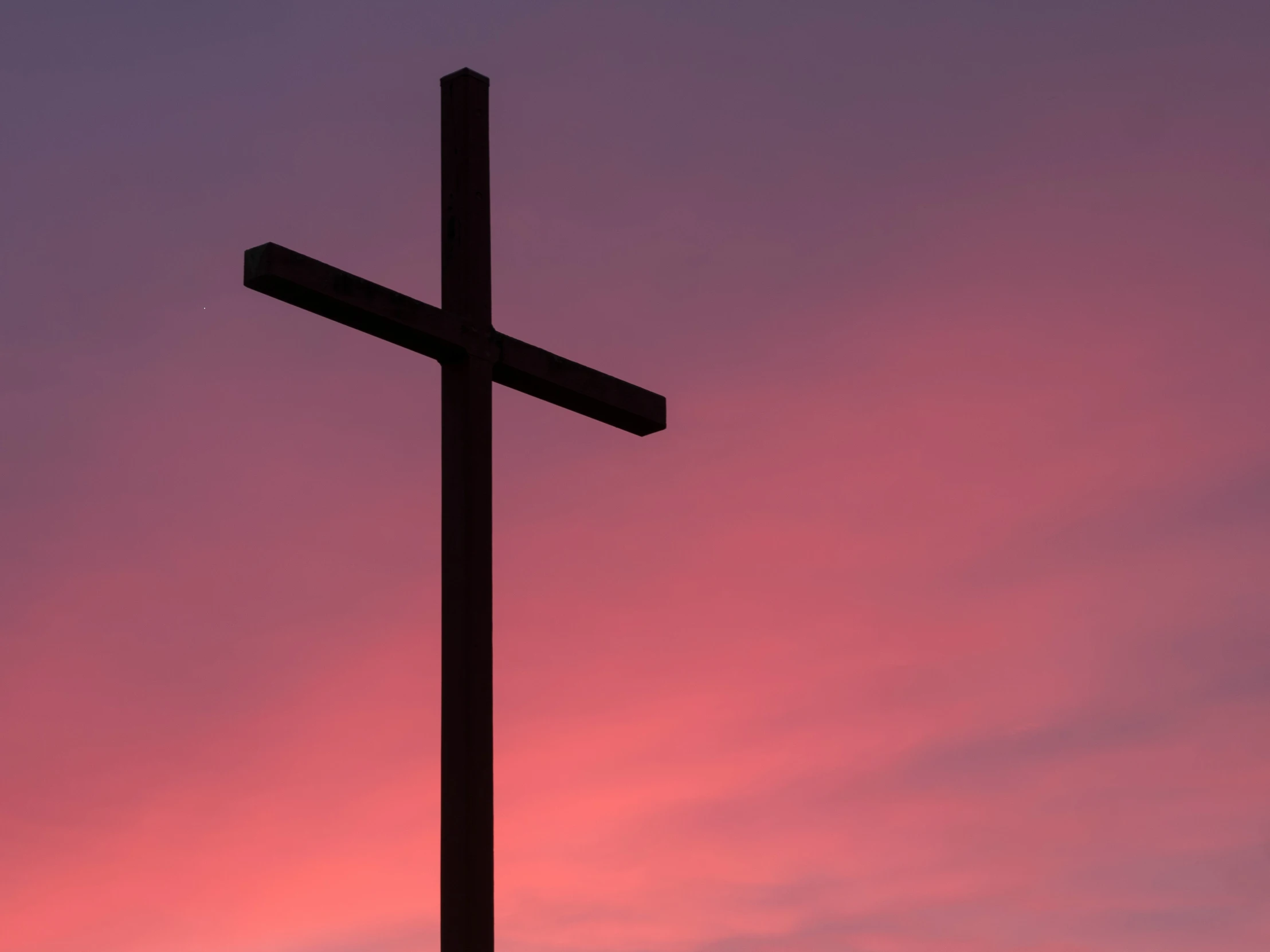 a cross silhouetted against a pink sunset sky