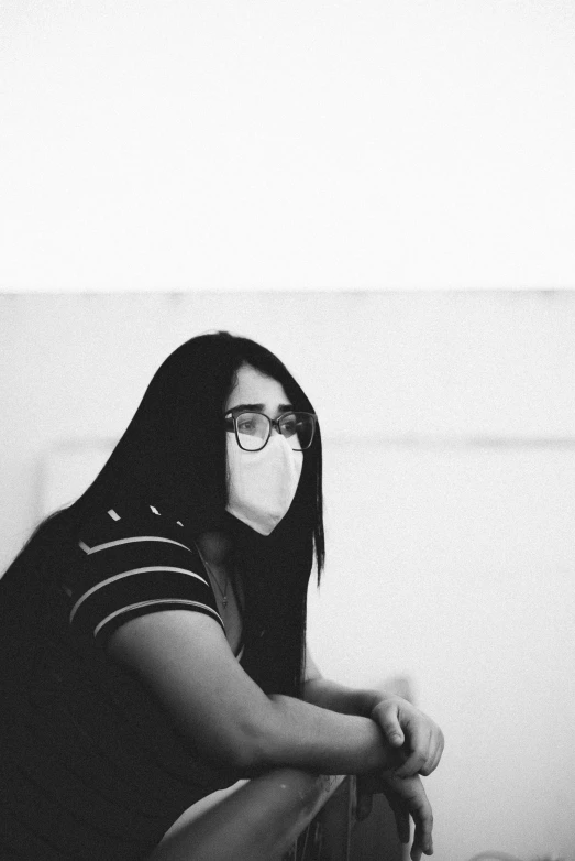 a girl sits against a wall wearing a mask