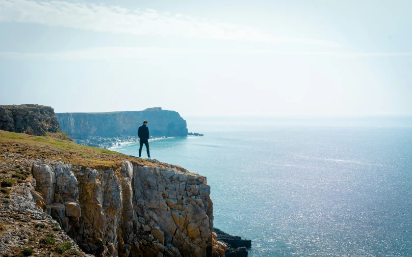 a man standing on top of a cliff overlooking the ocean