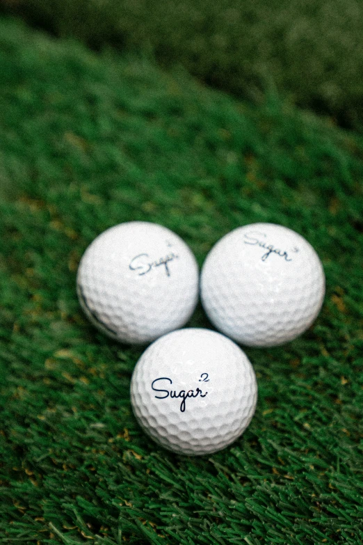 three golf balls and their name are on the grass