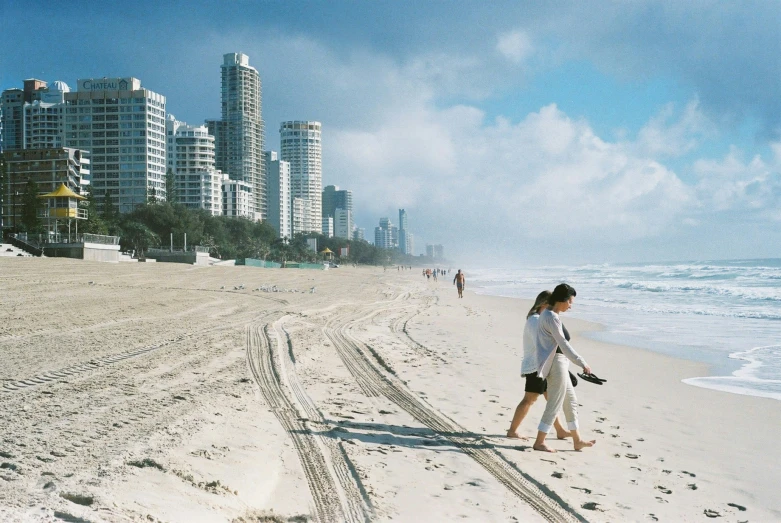 two people walking on the beach, looking out at a city