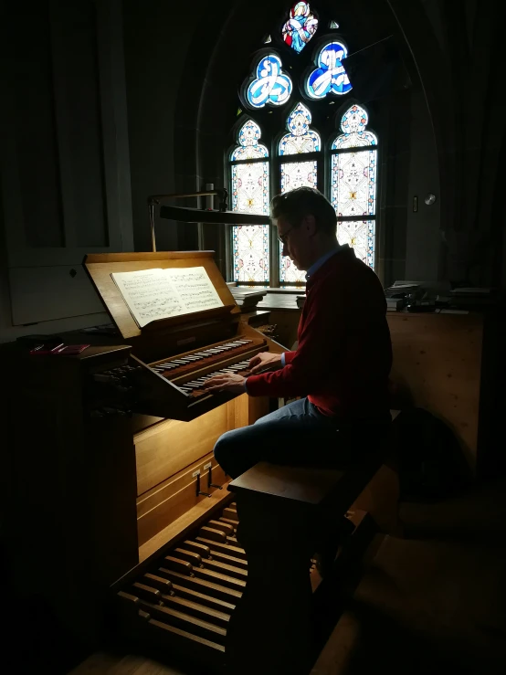 man playing an upright piano inside a gothic style building