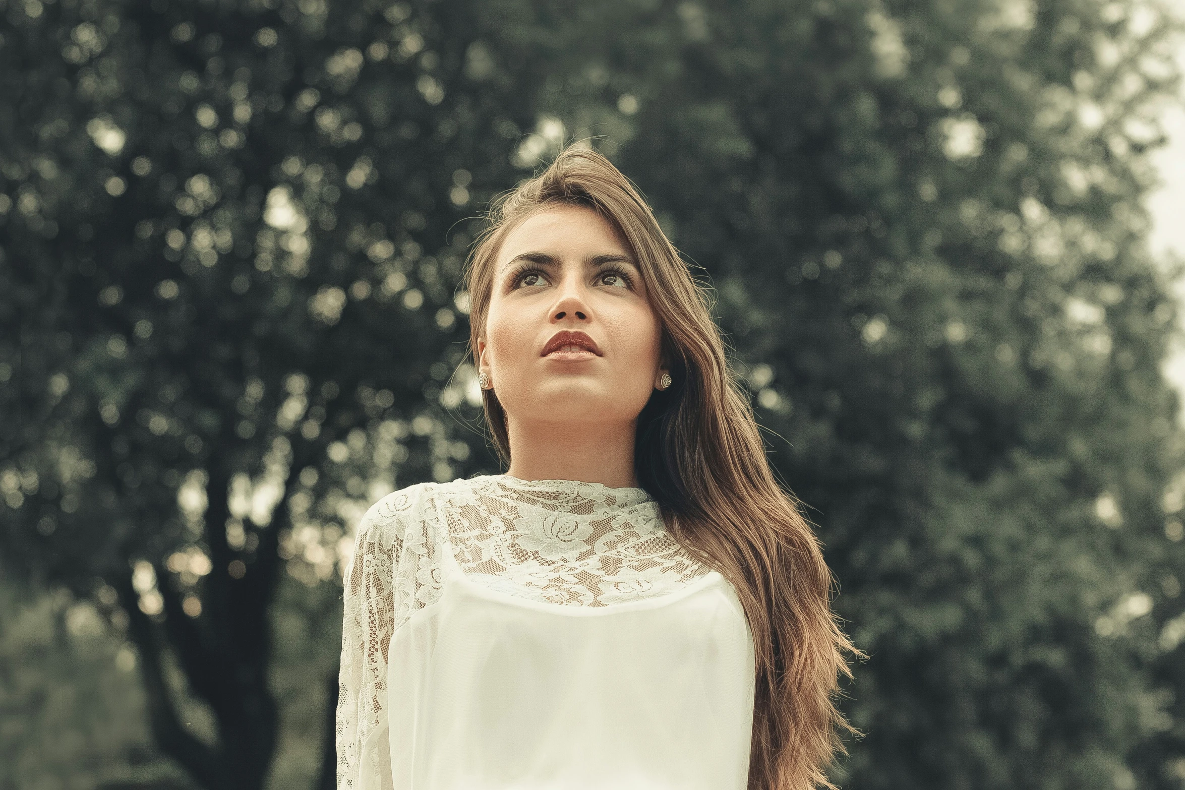 a woman with her eyes closed standing near trees