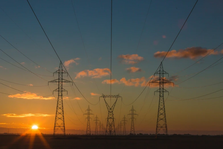 an orange sun is in the distance and some power poles