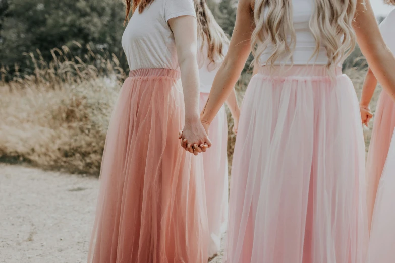 three women holding hands and wearing peach and white dress