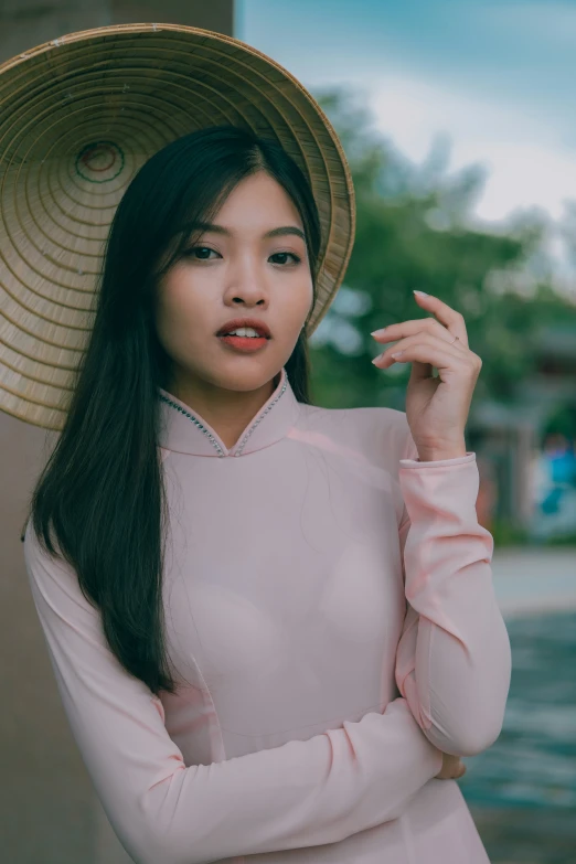 woman wearing pink shirt with long dark hair and large hat standing on sidewalk