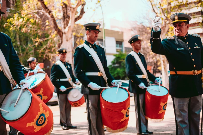 four men in uniform standing on a street near three drum bags