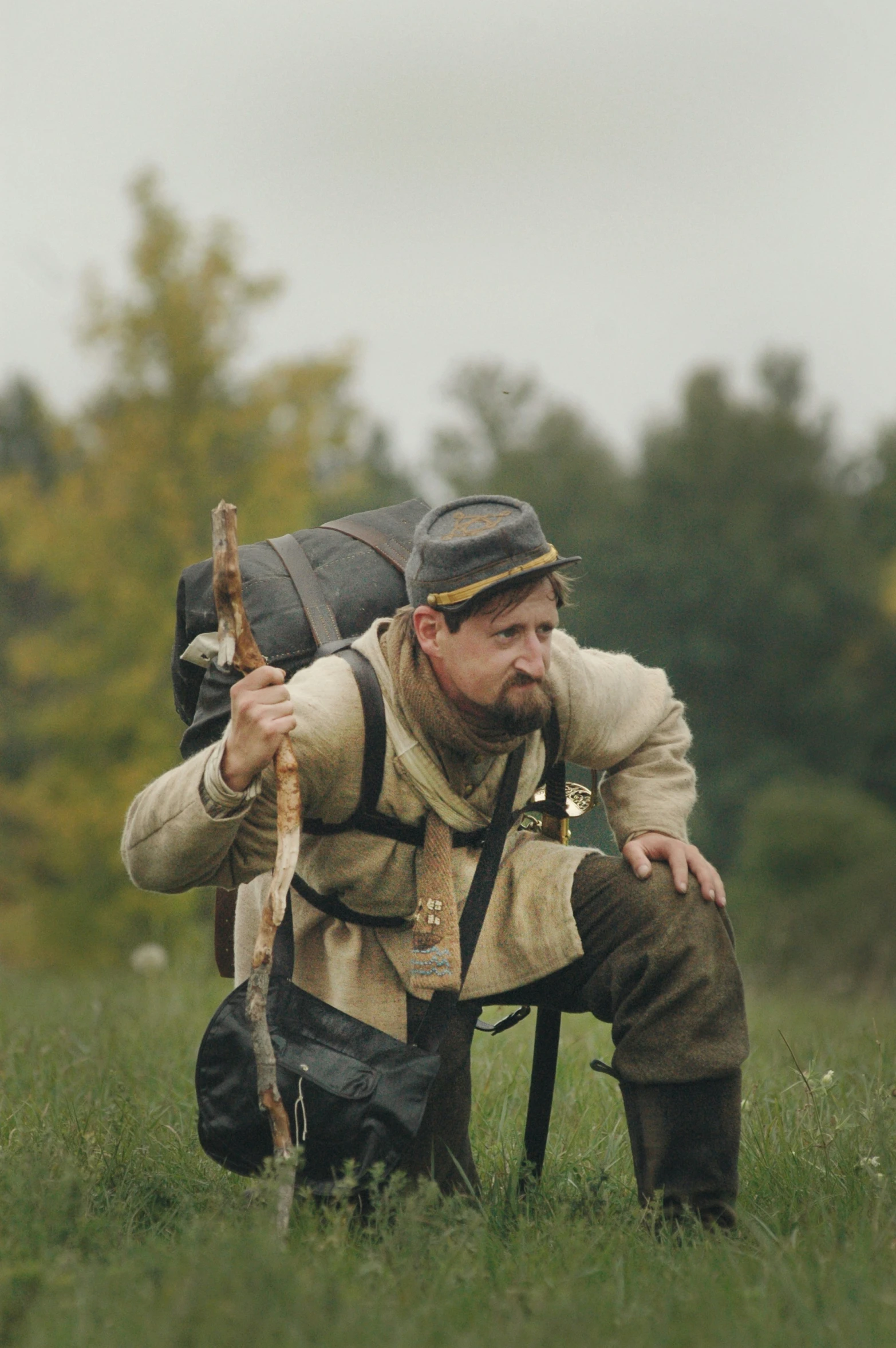 man holding a walking stick sitting on the ground with the backpack