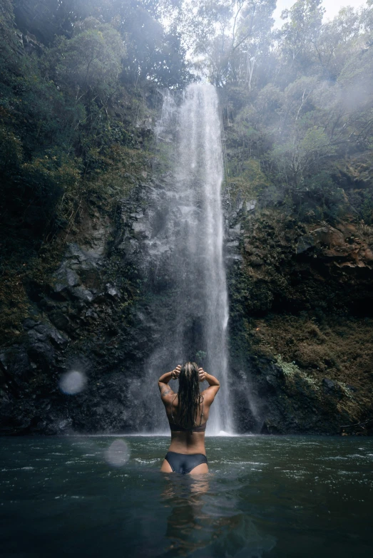 a person sitting in water next to waterfall