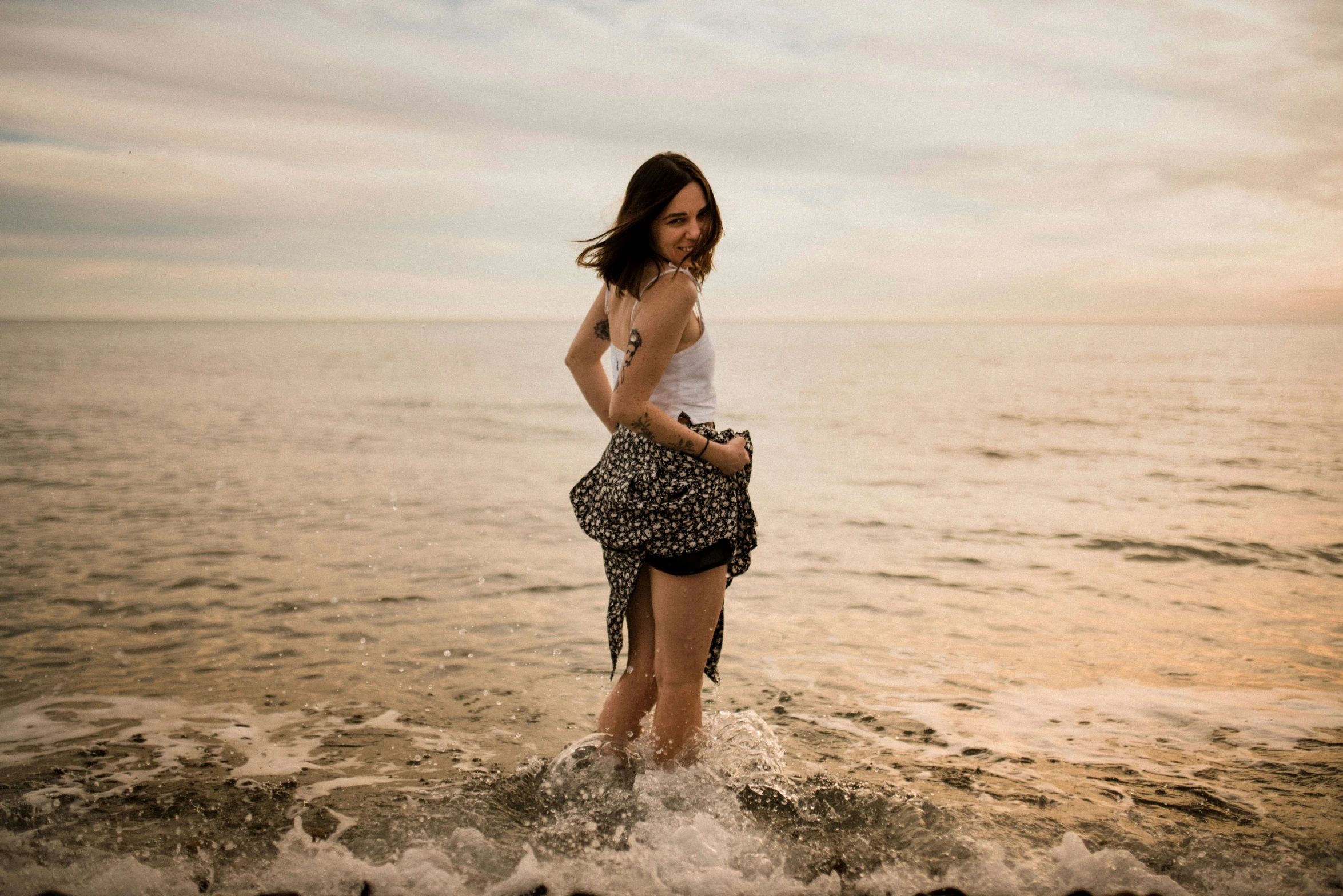 a woman standing on the ocean shore in a white tank top and black leopard print short