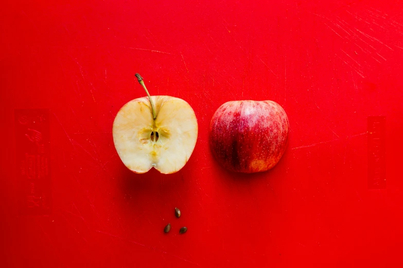 an apple and a pepper sitting on a red surface