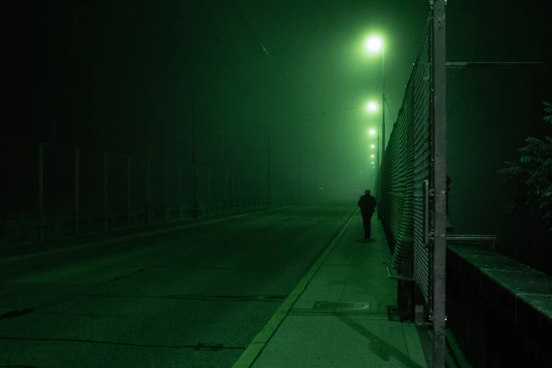 a person standing on a sidewalk in the dark with a green light