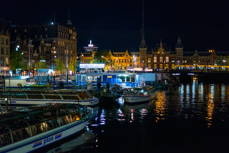 boats moored in a harbor at night near a city