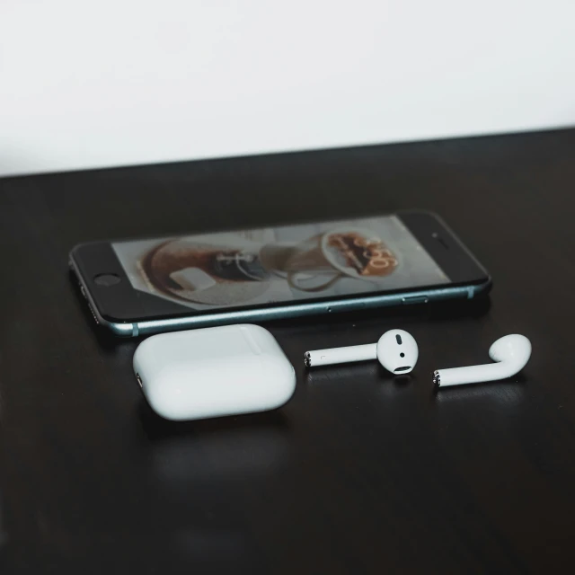 a black table has a cell phone with ear buds