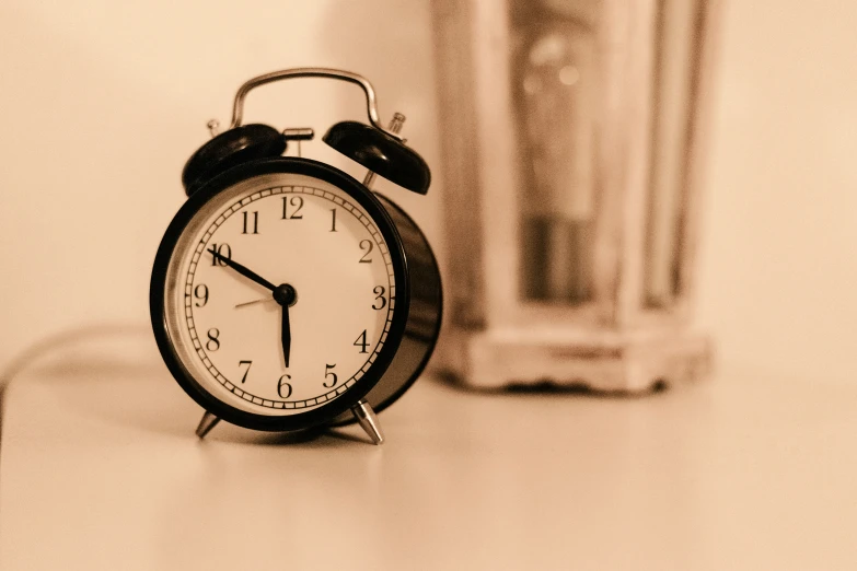 an alarm clock sits on a table near a glass