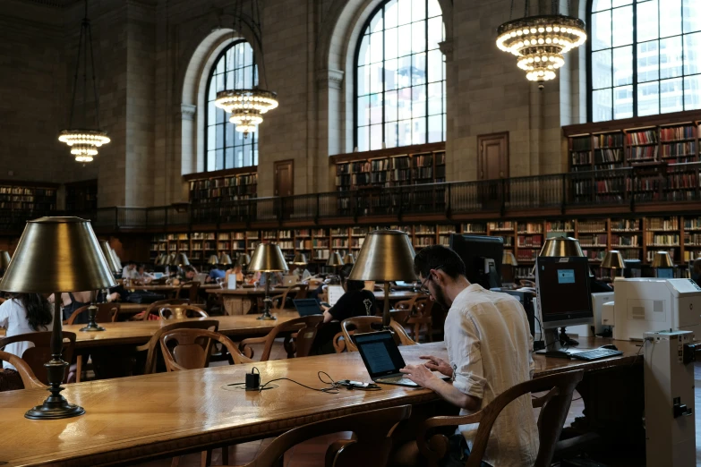 an old liry has multiple tables and lamps and people working on laptops