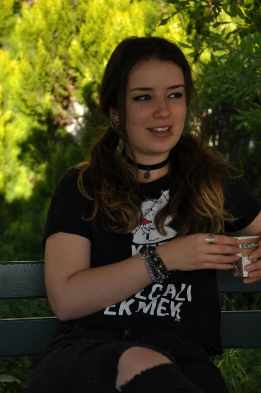 a girl with her arm around her shoulder and a drink sitting on a bench in front of a tree