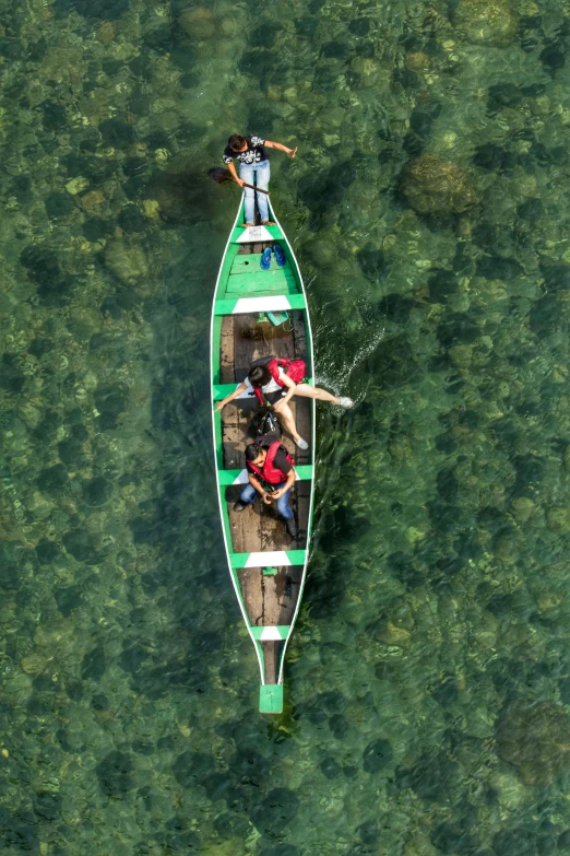 three people paddling in a green boat in clear water