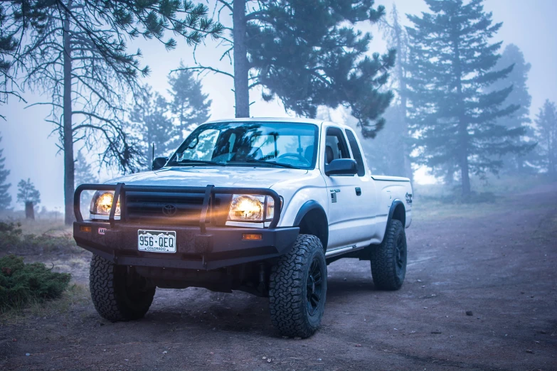 a truck driving down a dirt road by some trees