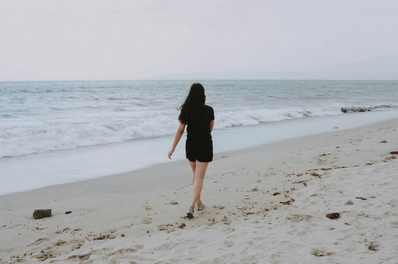 a woman in a black dress walking along a beach
