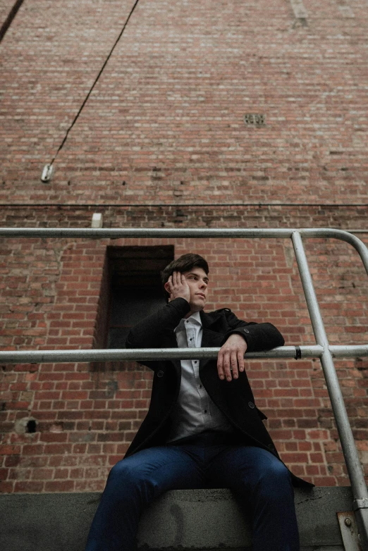 a young man is posing while sitting on a handrail