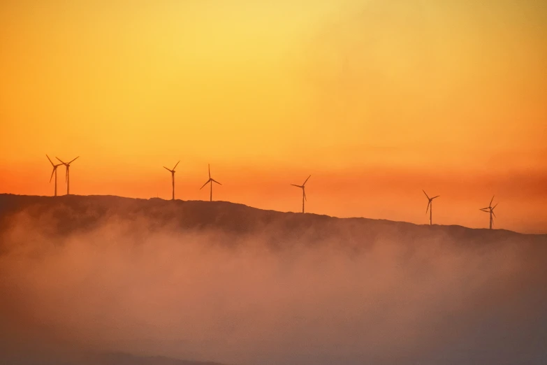 wind turbines stand on a hillside at sunset