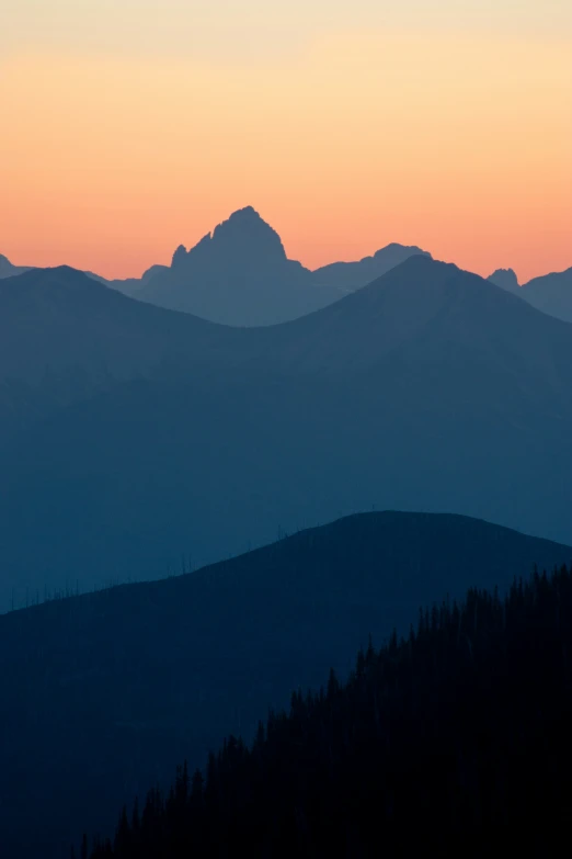 a sunset scene over mountains with some evergreen trees