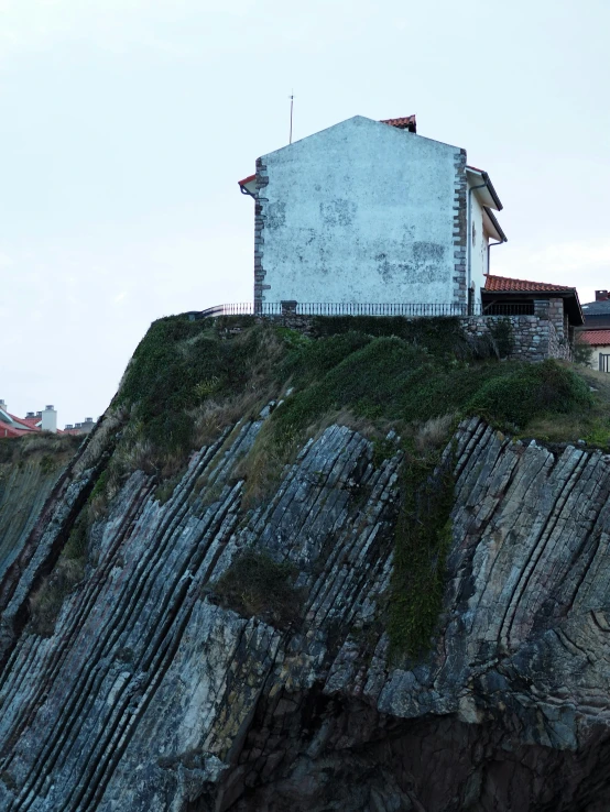 a house sits on a small cliff above the ocean