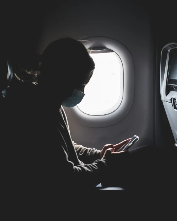 a man wearing a mask, sitting down in an airplane reading soing