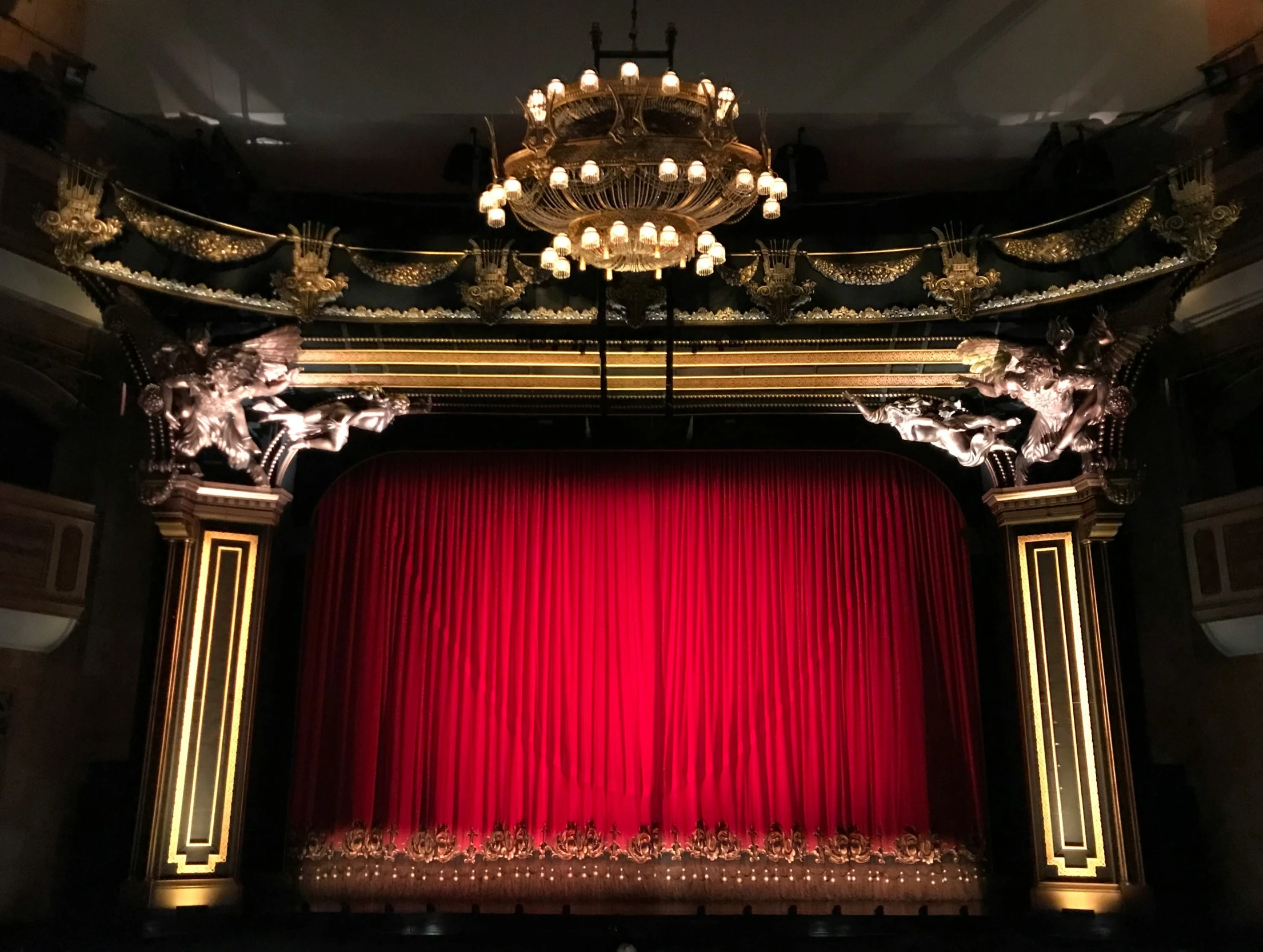 a stage with red curtain and chandelier