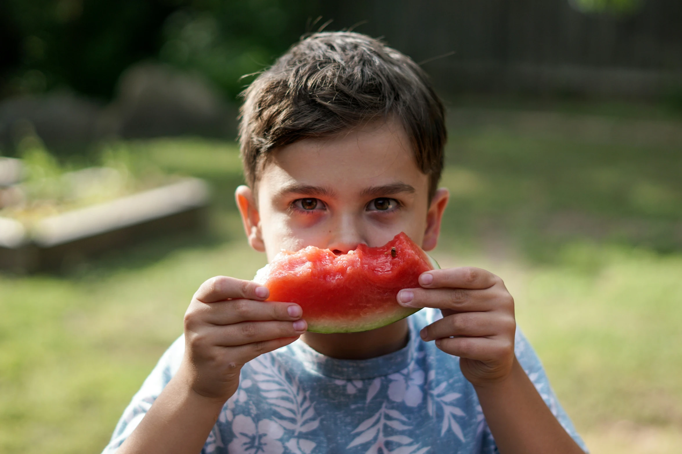 the boy is eating watermelon in the yard