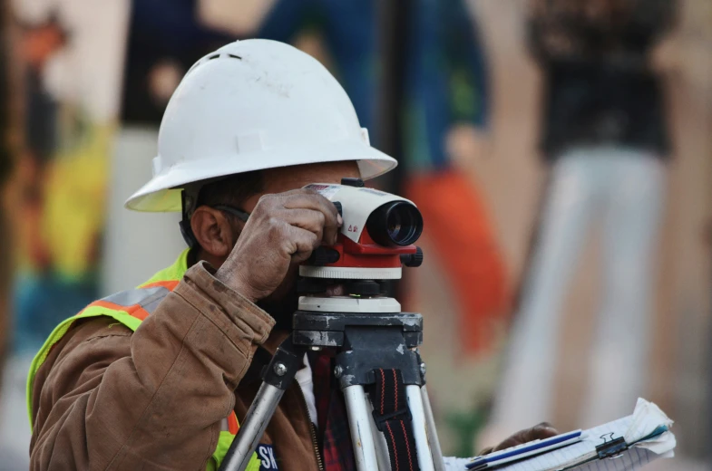 construction worker using tripod looking through binora while standing in front of a construction site