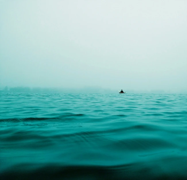 lone boat sailing in the sea with hazy sky