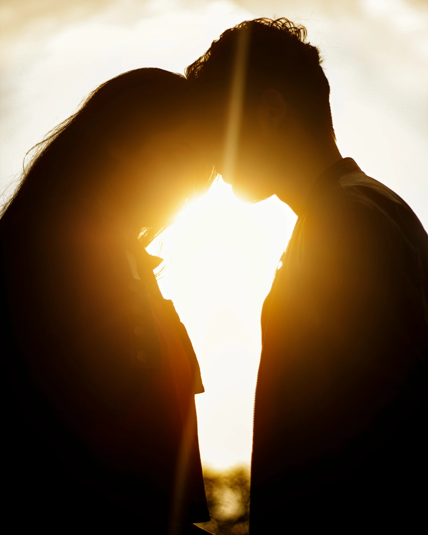 a couple is kissing in front of the setting sun