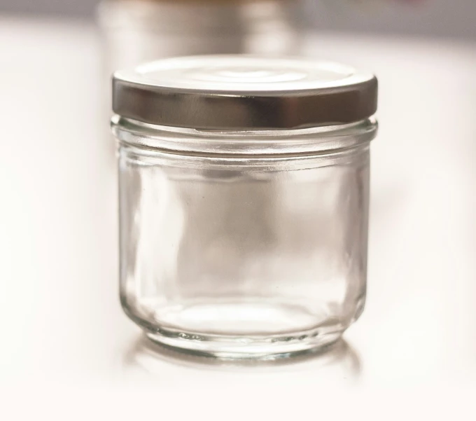 a glass jar with metal lid is sitting on a white surface