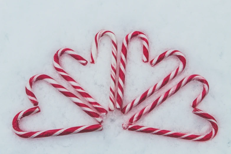 red and white candy canes laying on snow with two shaped like heart