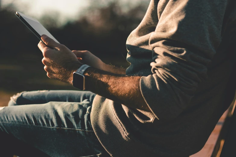 the man sitting on a bench is holding his ipad